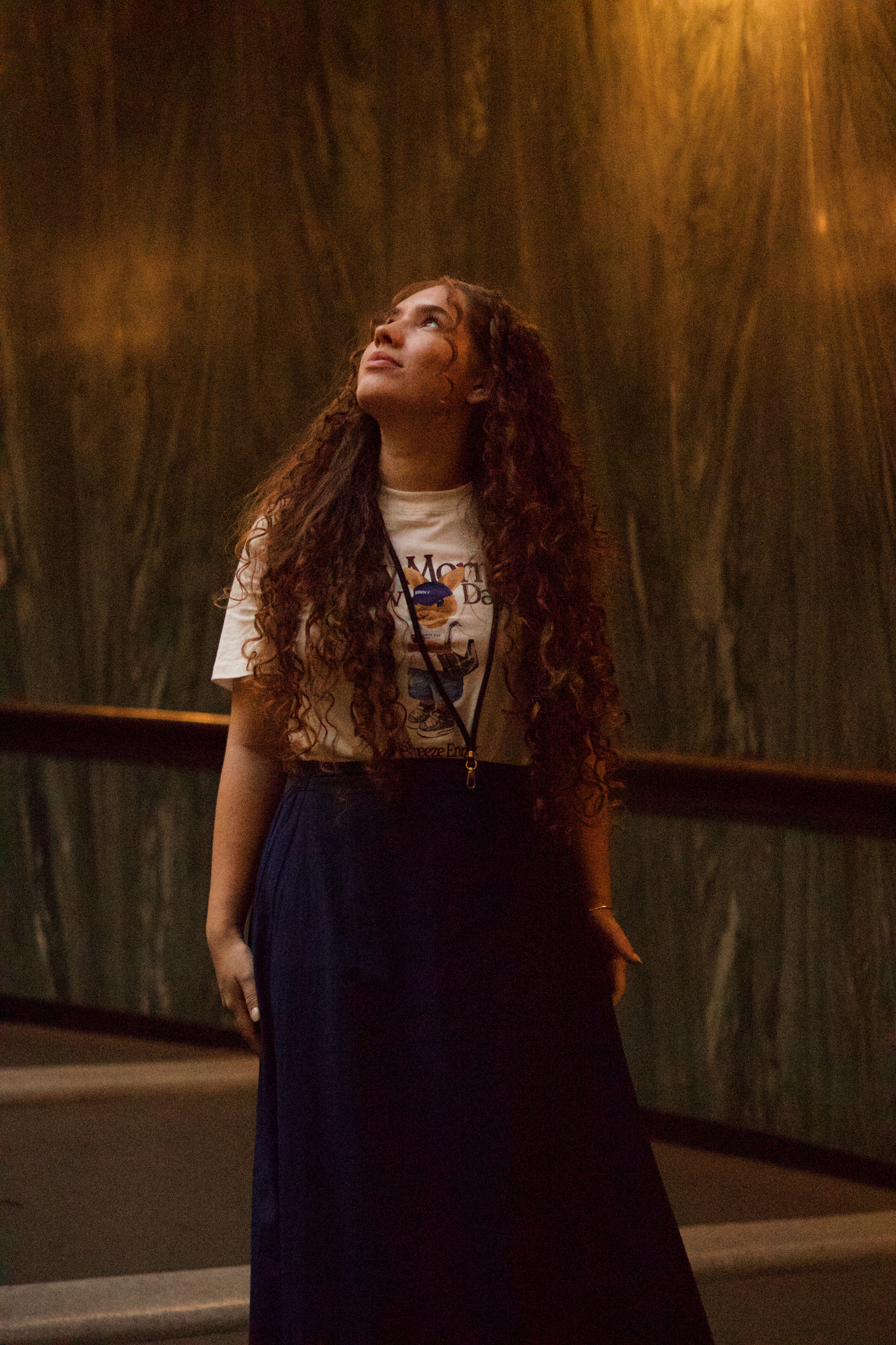 Beatriz em pé diante de uma parede iluminada por luz quente